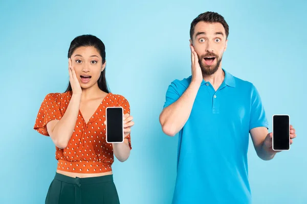 Shocked Interracial Couple Touching Faces While Holding Smartphones Blank Screen — Stock Photo, Image