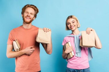 Sarışın ve kızıl saçlı öğrenciler ellerinde mavi torbalarla kitap taşıyorlar.