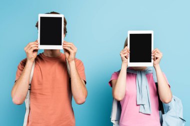 Mavi ekranda boş ekranlı dijital tabletleri tutarken yüzleri örten genç öğrenciler