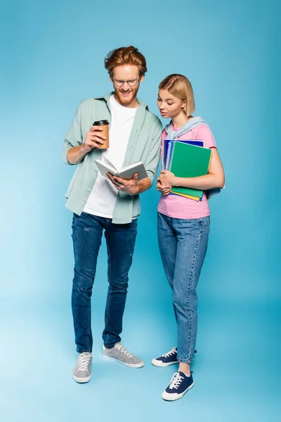 Mladí Studenti Čtení Knihy Zatímco Drží Kávu Jít Notebooky Modré — Stock fotografie