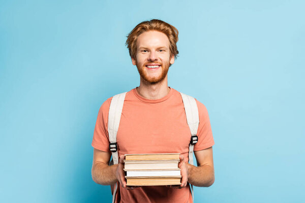 redhead student holding books and looking at camera on blue