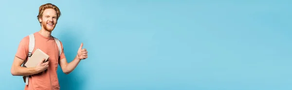 Панорамный Урожай Бородатого Студента Держащего Книгу Показывающего Большой Палец Голубом — стоковое фото
