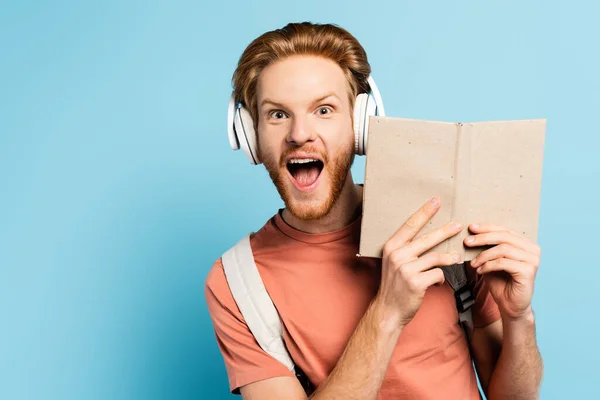 Excited Redhead Student Wireless Headphones Holding Book Blue — Stock Photo, Image