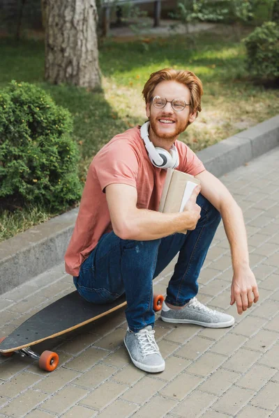 Бородатый Рыжий Студент Сидит Скейтборде Держит Книгу Снаружи — стоковое фото