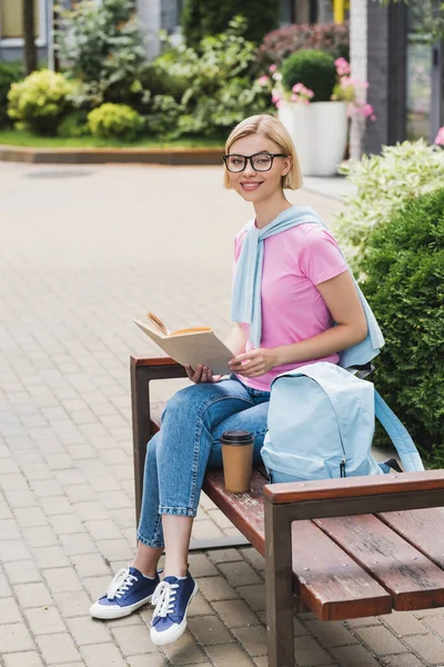 ブロンド学生で眼鏡をかけ本に座っている間にベンチ — ストック写真