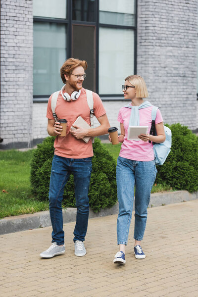 students in glasses holding coffee to go and looking at each other while walking outside 