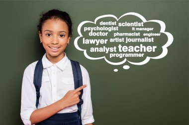 african american schoolgirl pointing with finger at green chalkboard with thought bubble and greeting lettering  clipart