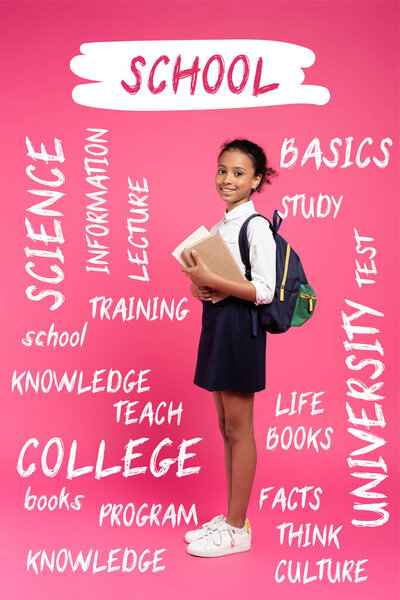 african american schoolgirl with backpack holding books near school lettering on pink 