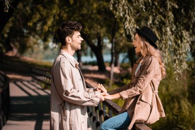 profile of man and woman in trench coats looking at each other in autumnal park clipart