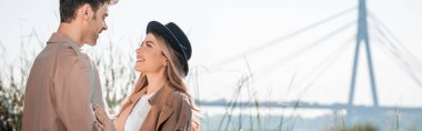 panoramic shot of woman in hat and man looking at each other outside clipart