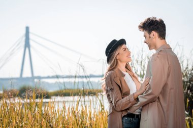 woman in hat and man embracing and looking at each other outside clipart