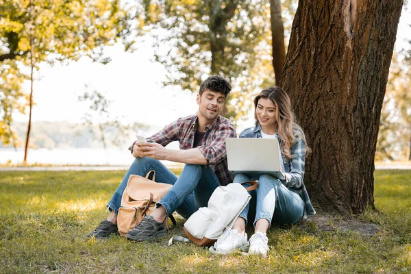 Férfi Gazdaság Smartphone Nézi Laptop Közelében Parkban — Stock Fotó