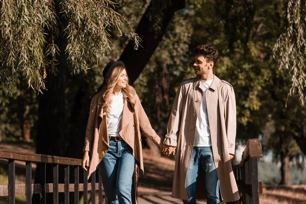 Couple Trench Coats Holding Hands Looking Each Other Walking Wooden — Stock Photo, Image