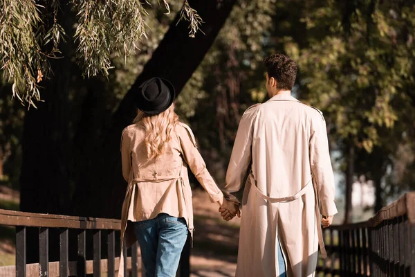 Vista Trasera Pareja Gabardina Tomados Mano Caminando Sobre Puente Madera — Foto de Stock