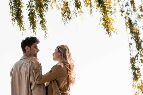 Ağacın yanındaki neşeli sevgiliye dokunan ve ona bakan sarışın kadın profili.