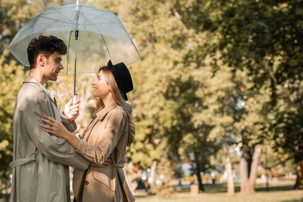 秋の公園の傘の下に立つトレンチコートの女性と男性の側面図 — ストック写真