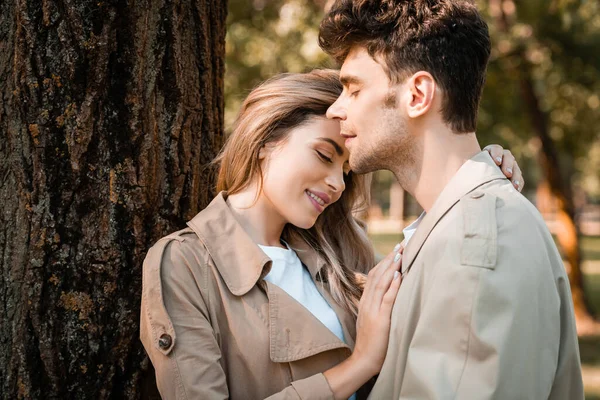 Pleased Woman Closed Eyes Hugging Man Trench Coat Tree Trunk — Stock Photo, Image