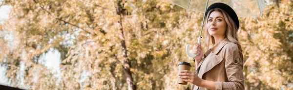 秋の公園に行くためにコーヒーと傘と紙コップを保持帽子のブロンドの女性のパノラマの概念 — ストック写真