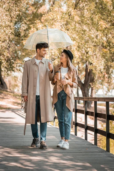 Couple Trench Coats Walking Wooden Bridge Umbrella Coffee — Stock Photo, Image