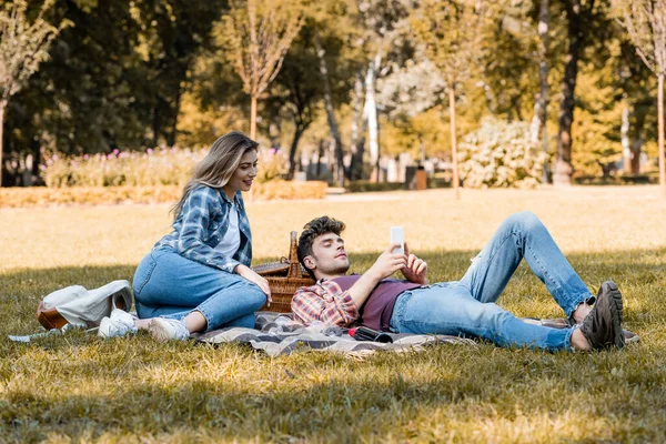 女人和男人在公园里躺在毛毯上看着智能手机 — 图库照片