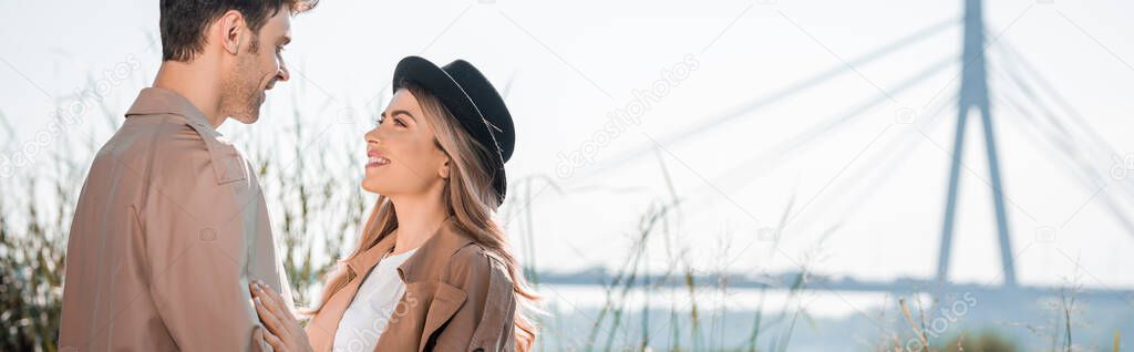 panoramic shot of woman in hat and man looking at each other outside