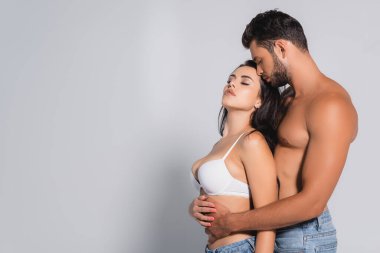 Ayakta duran kaslı adam gri sutyenli çekici kadını kucaklıyor.