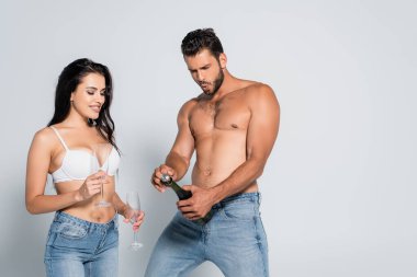 Kaslı adam, sütyenli, gri gözlüklü, baştan çıkarıcı kadının yanında şampanya şişesi açıyor.