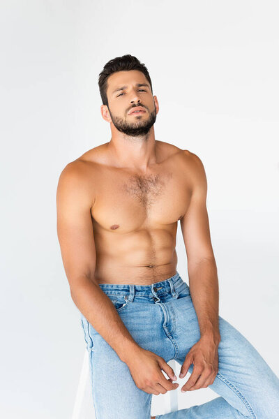 Мужчина без рубашки и бороды сидит в одиночестве на белом