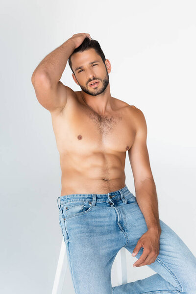 Мужчина без рубашки и бороды сидит и трогает волосы, изолированные на сером