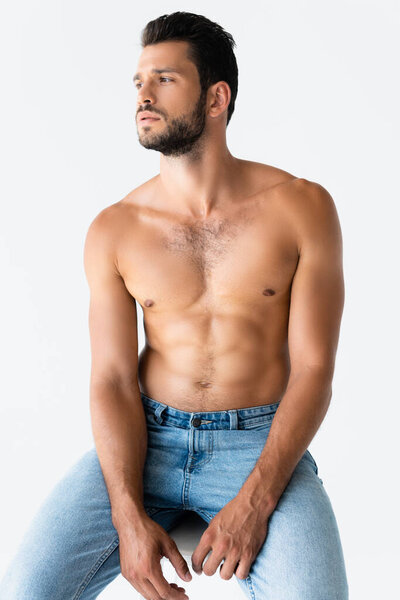 Мужчина без рубашки и бороды смотрит в сторону, сидя в одиночестве на белом