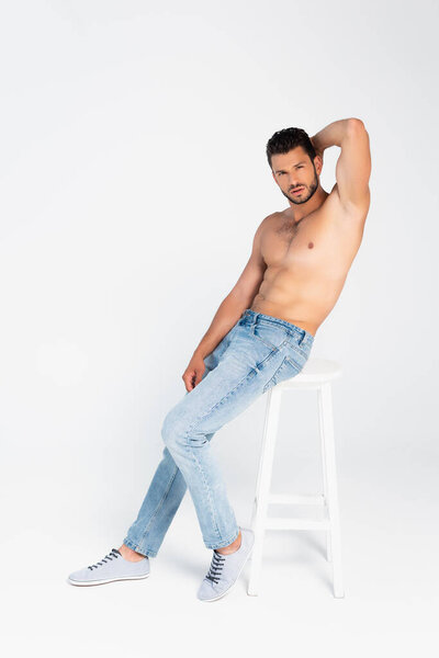 сексуальный мужчина сидит на стуле и смотрит в камеру на белом 