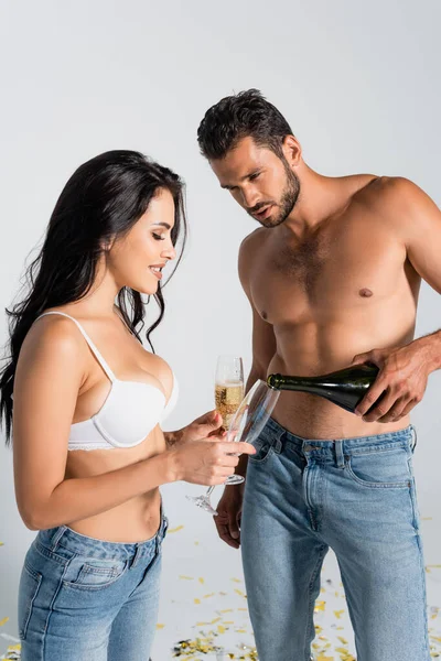 Kaslı adam bardağa şampanya dolduruyor. Yanında gri sutyenli seksi kadın var.