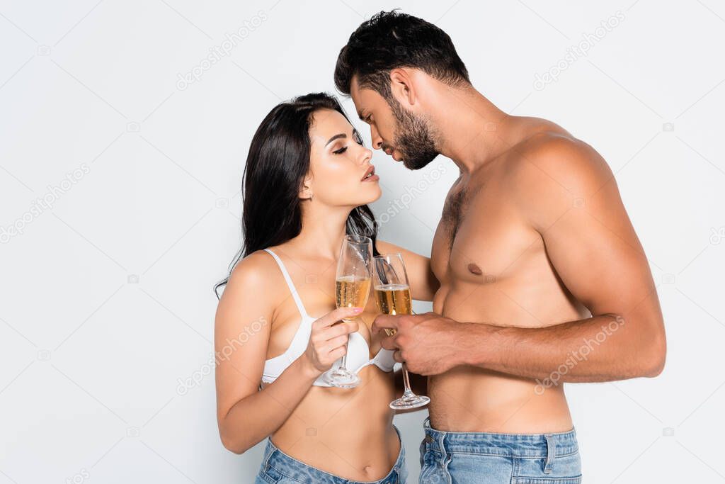 muscular man and seductive woman in bra holding glasses of champagne on grey