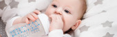 vízszintes koncepció csecsemő fiú kezében cumisüveg, miközben fekszik az ágyban
