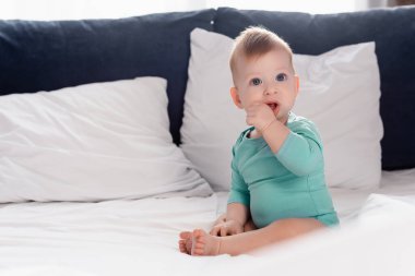 Bebek arabasında elleri ağızda, yatakta oturan erkek bebek odaklı.