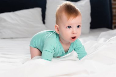 selective focus of infant boy in baby romper crawling in bed with open mouth clipart