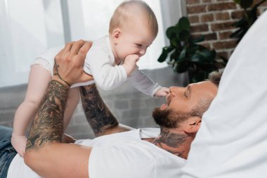 Yatakta yatarken kucağında bebek olan genç babanın yan görüntüsü.