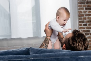 Evde otururken bebeği tutan dövmeli adamın seçici odak noktası.