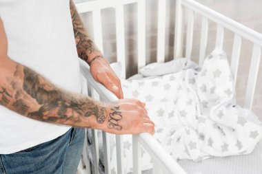 Evdeki beşiğin yanında duran dövmeli adam manzarası.