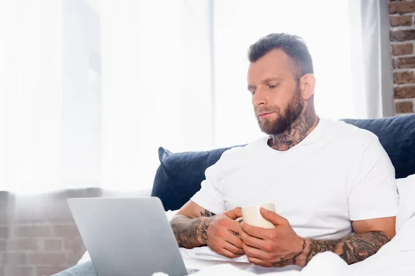 Young Tattooed Freelancer Using Laptop While Sitting Bedroom Cup Tea — Stock Photo, Image