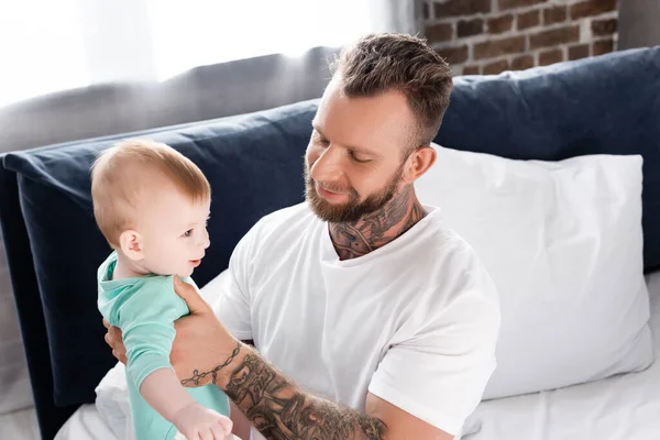 Mladý Otec Bílém Tričku Drží Dítě Zatímco Sedí Posteli — Stock fotografie