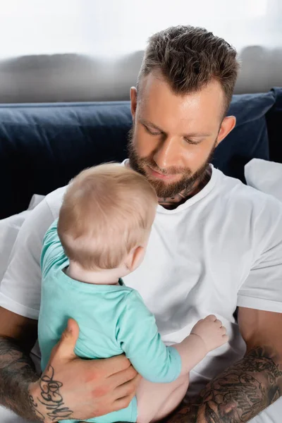 Young Tattooed Father Holding Baby Boy While Sitting Bedroom — Stock Photo, Image