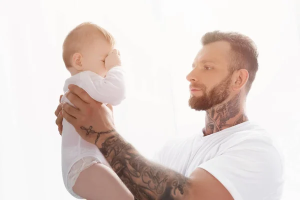 赤ちゃんを抱えた若い入れ墨の男が目に触れる — ストック写真