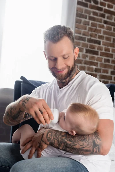 Young Tattooed Man Feeding Infant Boy Baby Bottle Home — Stock Photo, Image
