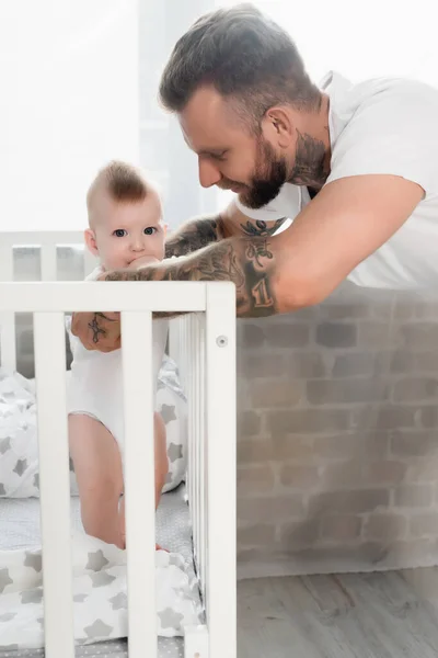 Tatuerad Man Som Stöder Spädbarn Som Står Barnsäng Och Håller — Stockfoto