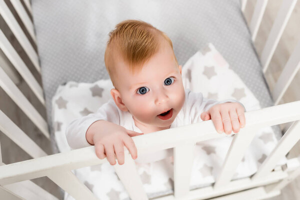 overhead view of infant boy looking at camera while standing in crib