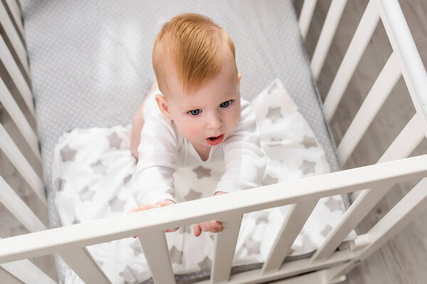 overhead view of infant boy standing in crib