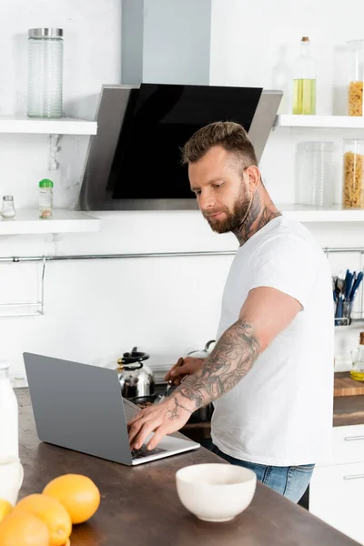 Jovem Barbudo Freelancer Shirt Branca Usando Laptop Perto Laranjas Tigela — Fotografia de Stock