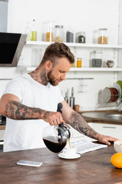Dövmeli Beyaz Tişörtlü Adam Gazete Okuyor Mutfak Masasında Cep Telefonunun — Stok fotoğraf