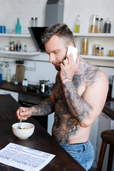 Svalnatý Potetovaný Muž Čtoucí Noviny Mluvící Smartphonu Během Snídaně Kuchyni — Stock fotografie